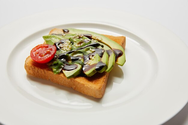 Messa a fuoco selettiva di pane tostato con avocado e pomodorini su piatto bianco