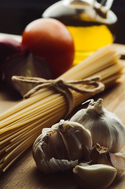 Messa a fuoco selettiva di spicchi d'aglio separati vicino al bulbo. Mazzetto di spaghetti e verdure con olio in bottiglia