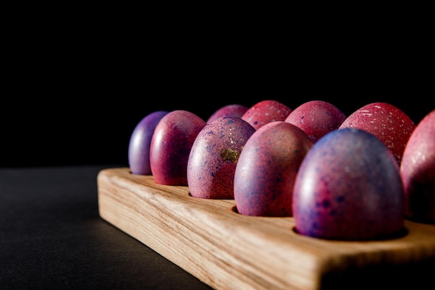 Messa a fuoco selettiva di uova di Pasqua colorate su tavola di legno su sfondo grigio e nero