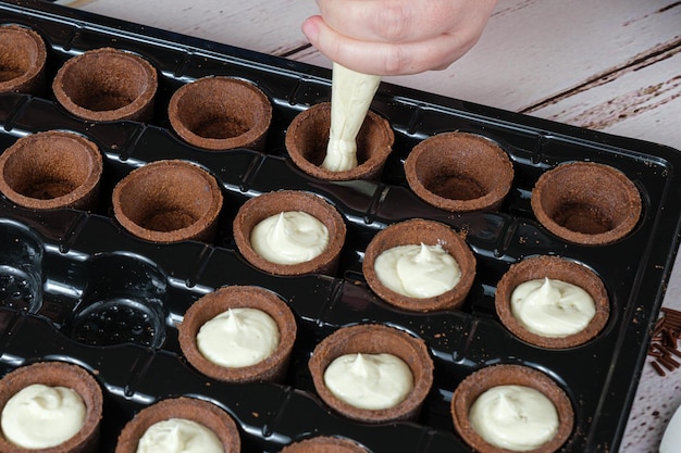 Messa a fuoco selettiva. Primo piano dell'ugello del pasticcere che riempie la mini ganache al cioccolato bianco con crostate al cioccolato.