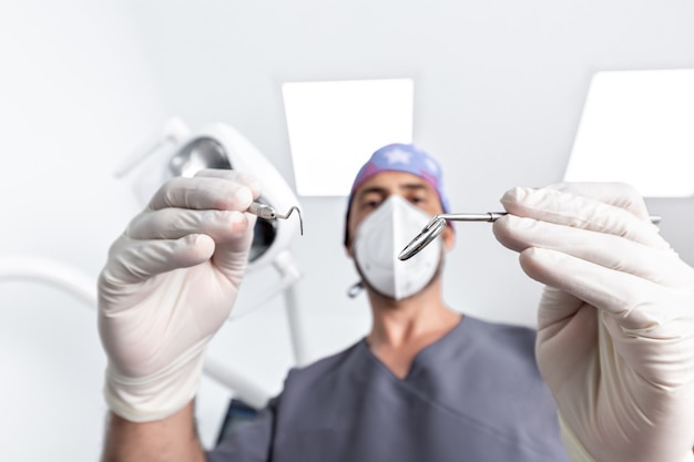 Messa a fuoco selettiva sugli strumenti che utilizzano un dentista maschio con uniforme e maschera in una clinica odontoiatrica