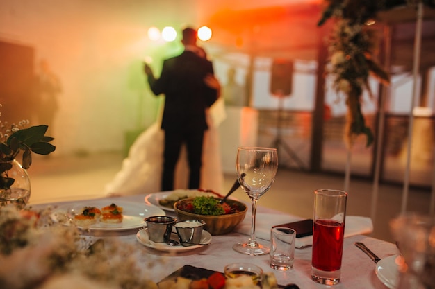 Messa a fuoco selettiva sul tavolo delle nozze con bevande e cibo sullo sfondo sposini che ballano il primo ballo