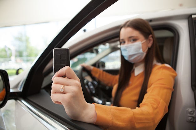 Messa a fuoco selettiva sulla chiave dell'auto sulla mano della guidatrice che indossa una maschera medica durante la pandemia di coronavirus