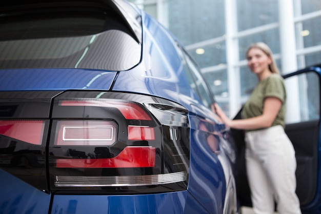 Messa a fuoco selettiva sulle luci dell'auto, donna che esamina l'auto presso la concessionaria auto