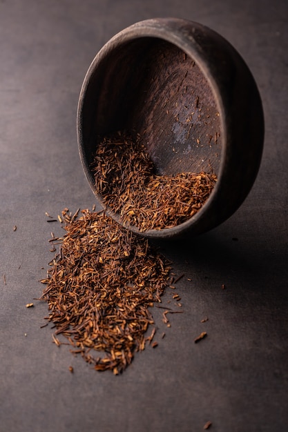 Messa a fuoco selettiva, tè rosso naturale in foglia, preparazione in una macro di angolo verticale di una ciotola di legno su un backgrou chiaro...