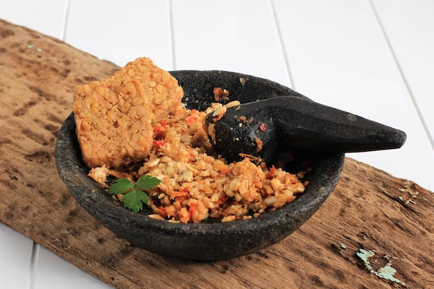 Messa a fuoco selezionata Sambal Tempeh, Tempe schiacciato piccante su pestello di pietra. Cibo tradizionale indonesiano con gusto piccante e salato