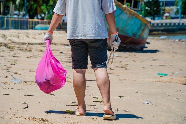 Messa a fuoco Uomo volontario che indossa guanti che raccolgono i rifiuti delle bottiglie sulla spiaggia del parco Pulizia della natura