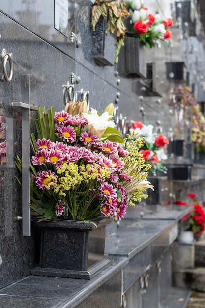 Messa a fuoco verticale poco profonda di mazzi di fiori sotto lapidi di marmo scuro al cimitero