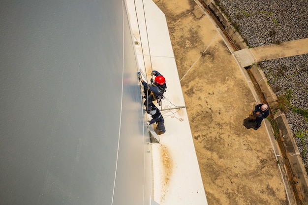 Messa a fuoco vista dall'alto lavoratore di sesso maschile in basso altezza serbatoio tetto accesso alla fune ispezione di sicurezza dello spessore del serbatoio di stoccaggio gas propano.