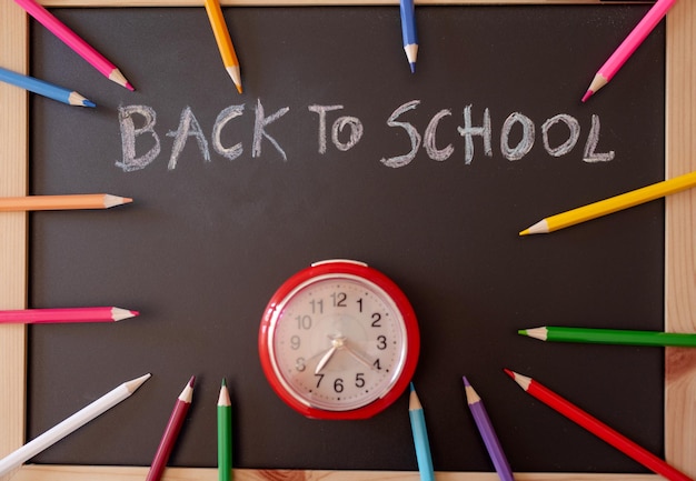 messaggio di ritorno a scuola sulla lavagna con un orologio e matite colorate intorno