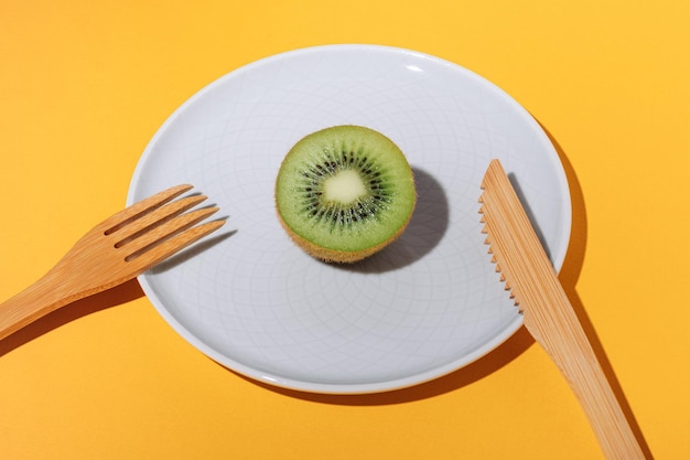 Metà del kiwi maturo succoso su un piatto e forchetta e coltello di bambù su un fondo giallo