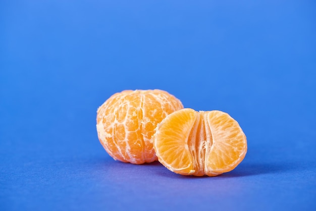 Metà del mandarino sbucciato vicino a tutta la clementina su sfondo blu