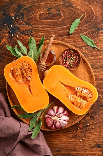 Metà della zucca butternut organica cruda con foglia di salvia, aglio pepe multicolore, miele, sale e pepe su fondo di legno vecchio. Sfondo di cibo. Vista dall'alto con copia spazio.