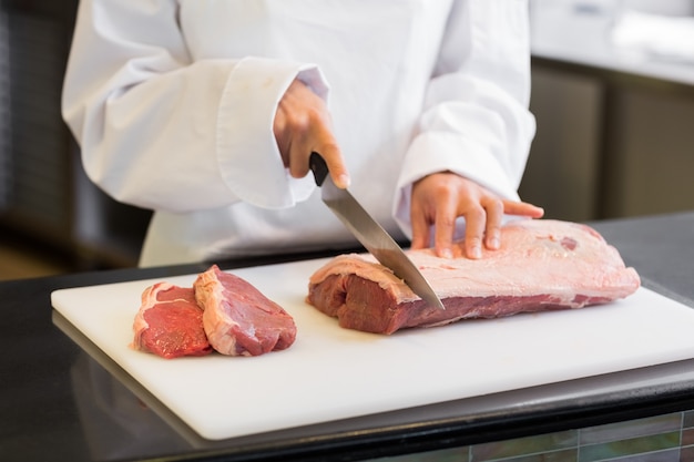 Metà di sezione delle mani che tagliano carne in cucina