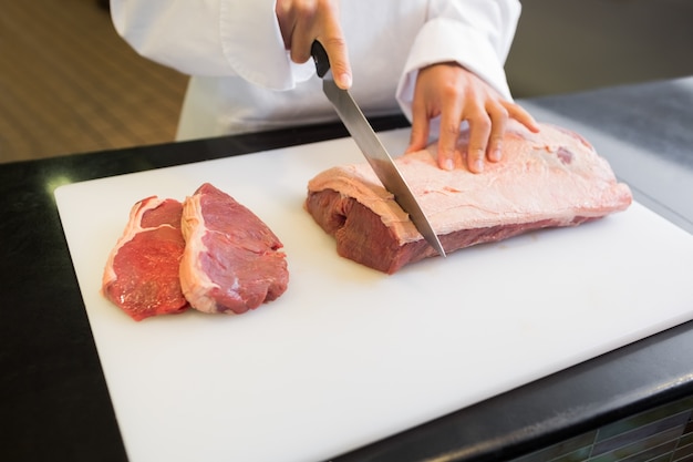 Metà di sezione delle mani che tagliano carne in cucina
