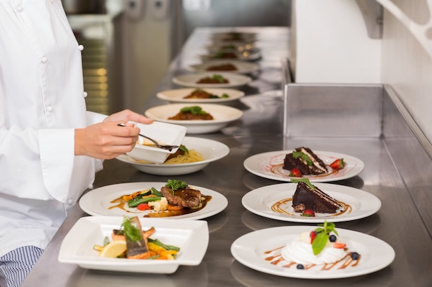 Metà di sezione di un cuoco unico femminile che guarnisce alimento in cucina