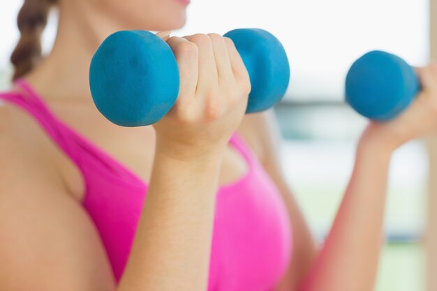 Metà di sezione di una donna che si esercita con i dumbbells nello studio di forma fisica