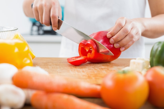 Metà di sezione di una donna che taglia le verdure a pezzi in cucina