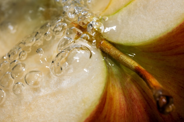 Metà di una mela dolce matura rossa sotto un flusso di acqua pulita macrofotografia ravvicinata