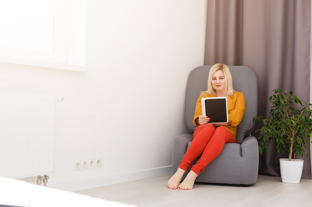 metà donna adulta seduta sul divano con tablet pc. Forma orizzontale, vista frontale, copia spazio