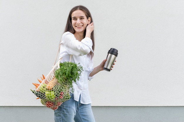 Metà donna del colpo che tiene borsa riutilizzabile e thermos fuori