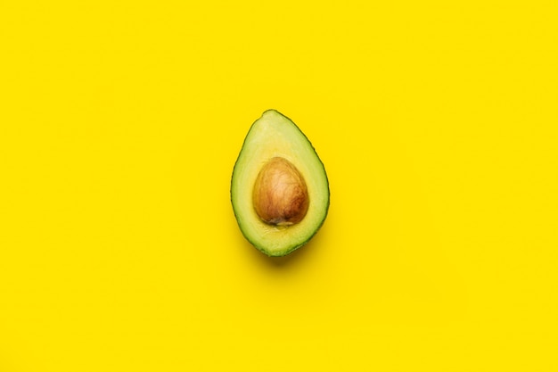 Metà matura fresca di un avocado con un osso su un giallo brillante