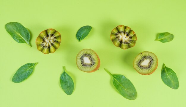 Metà verdi verdi del kiwi e foglie degli spinaci su un fondo verde, vista superiore, monocromatico, insegna