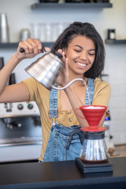 Metodo di fermentazione filtrata. Sorridente giovane donna graziosa che fa il caffè utilizzando pourover nella caffetteria