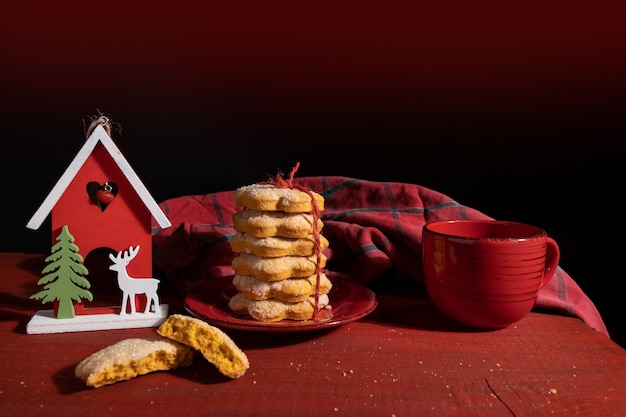 Metta i biscotti sulla tavola di legno rossa con la tazza di caffè rossa e il giocattolo del nuovo anno