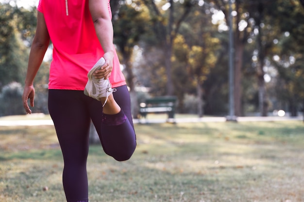 Metta in mostra la donna che allunga il muscolo della gamba che prepara per correre nel parco pubblico