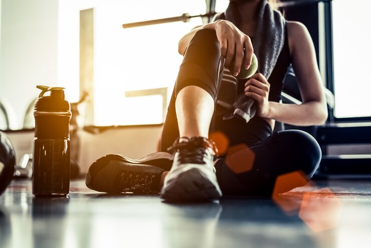 Metta in mostra la donna che si siede e che riposa dopo l&#39;allenamento o l&#39;esercizio nella palestra di forma fisica con la proteina shak