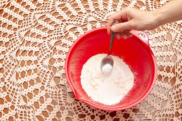 Mettere a mano lo zucchero con un cucchiaio in una ciotola di plastica rossa con la farina di frumento