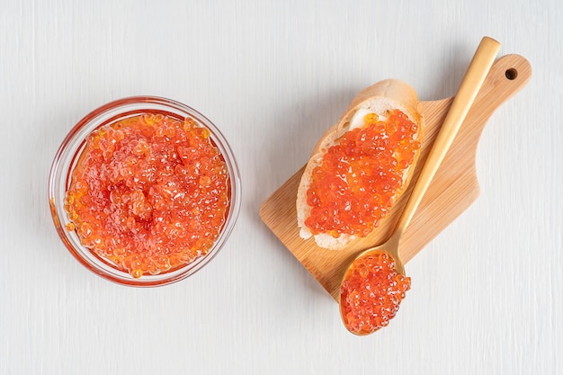 mettere piatto con caviale rosso o uova di pesce su una fetta di cucchiaio di pane e in una ciotola su uno sfondo bianco di legno