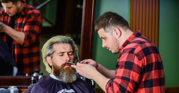 Metti alla prova il tuo viso e ottieni una forma perfetta uomo barbuto che si fa tagliare la barba da barbiere baffi e barba seduti sulla sedia dal parrucchiere uomo maturo dal parrucchiere Cura dei capelli e concetto di toelettatura maschile