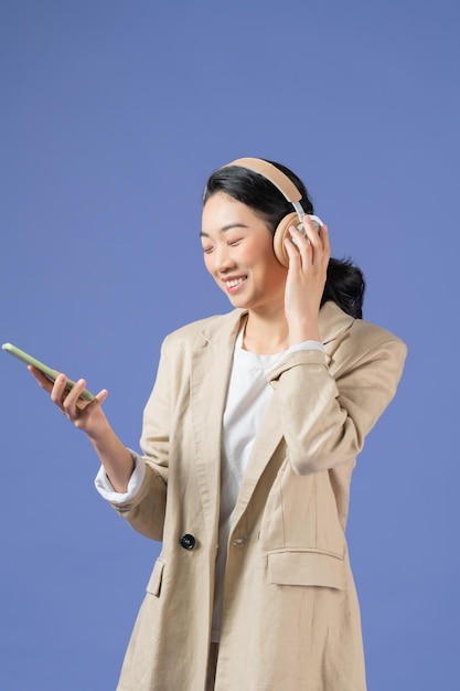 Mezza lunghezza della giovane signora sorridente con gli auricolari che distoglie lo sguardo tenendo il telefono cellulare in braccio