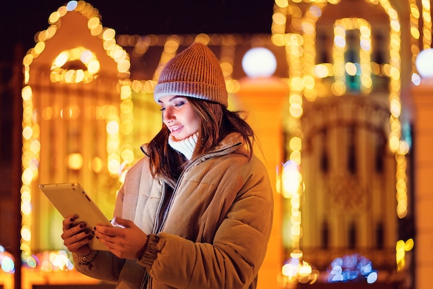 Mezza lunghezza della ragazza sorridente usa la sua tavoletta digitale mentre sta in piedi le vacanze di Natale all'aperto