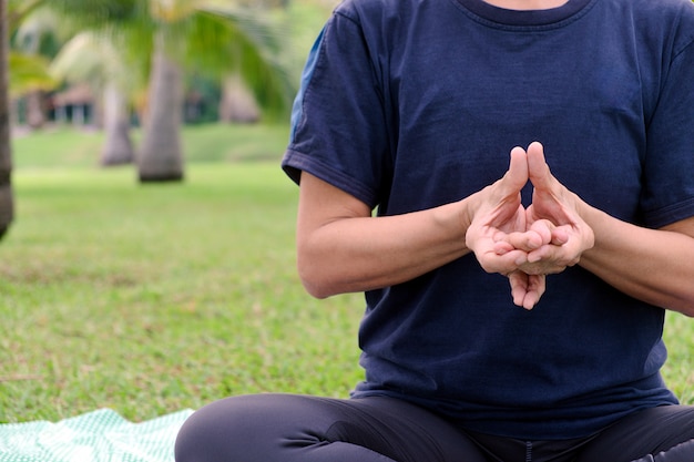 Mezza parte del corpo del primo piano della donna asiatica che gioca la pratica di yoga con la posizione di piegamento del dito sul parco pubblico di mattina