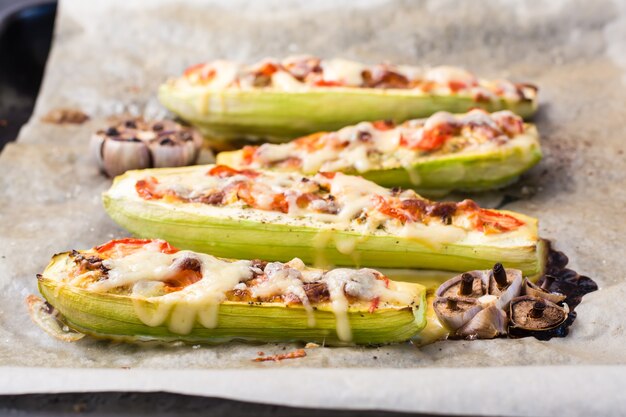 Mezze zucchine al forno pronte ripiene di formaggio e pomodoro su carta da forno su una teglia. Piatti di verdure, cibo sano. Avvicinamento