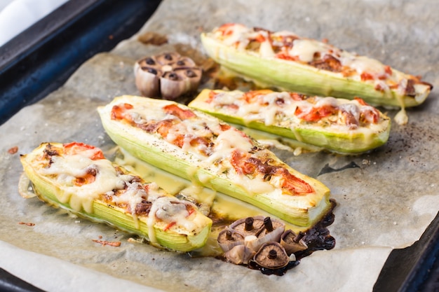 Mezze zucchine al forno pronte ripiene di formaggio e pomodoro su carta da forno su una teglia. Piatti di verdure, cibo sano