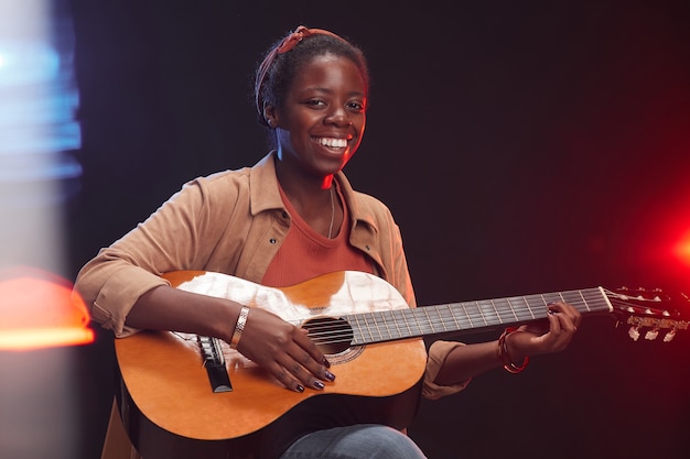 Mezzo busto ritratto di giovane donna afro-americana a suonare la chitarra sul palco e sorridente, copia spazio