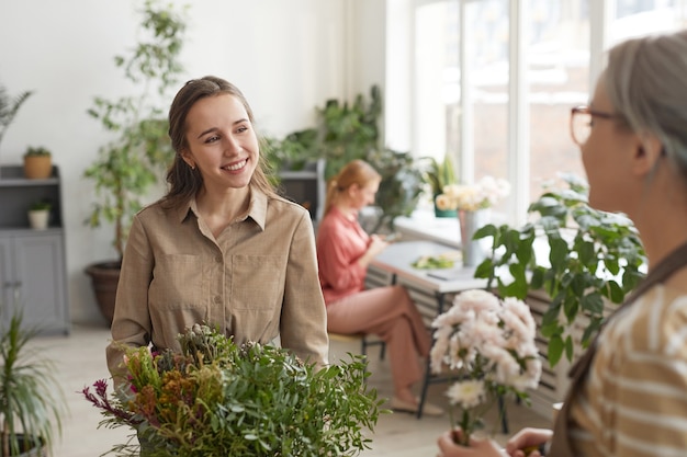 Mezzo busto ritratto di giovane fiorista femminile che sorride felicemente mentre si gode il lavoro in un negozio di fiori, copia spazio