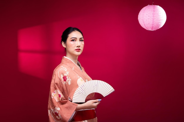 Mezzo corpo La giovane donna asiatica giapponese degli anni '20 indossa il tradizionale Kimono rosa con ventola d'arte e lampada