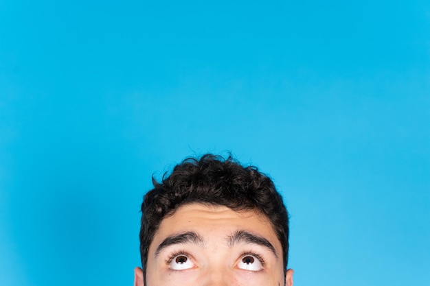 Mezzo ritratto di ragazzo adolescente ispanico che osserva in su per copiare lo spazio isolato su sfondo blu