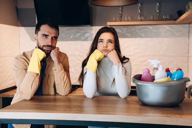 Mi chiedo coppia facendo pulizia della casa in cucina moderna a casa. Foto di giovane e bella donna che lava con detersivo e con la moglie