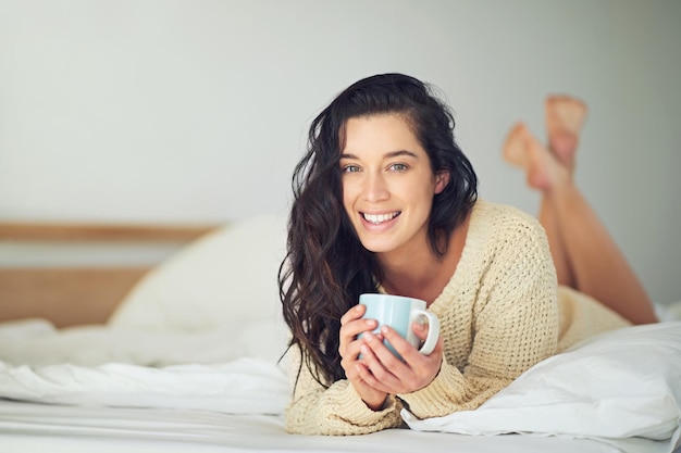 Mi faccio strada nel fine settimana Ritratto a figura intera di una giovane donna che beve caffè mentre è sdraiata sul letto