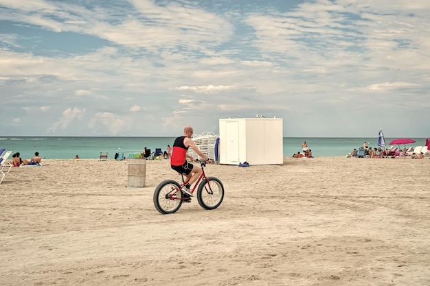 Miami USA 10 gennaio 2016 uomo o motociclista in bicicletta sulla spiaggia sud lungo la costa blu del mare o dell'oceano in una giornata di sole idilliaca sul cielo nuvoloso Vacanze estive Sport e stile di vita attivo