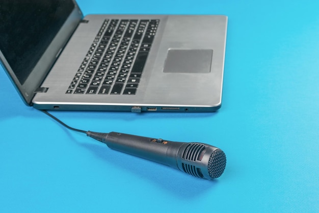 Microfono con un filo vicino a un laptop aperto su sfondo blu