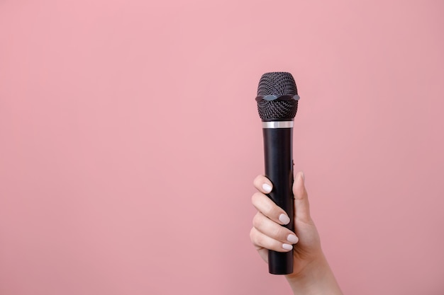 Microfono in mano femminile su sfondo rosa