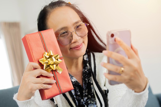 Middle age Asian woman using smartphone take a selfie with Christmas gift
