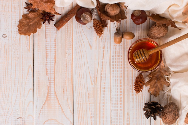 Miele, bastoncino, barattolo, sciarpa, foglie secche. Foto dolce rustica di autunno, fondo di legno bianco, copyspace.